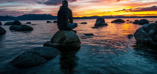 person sitting on rock on body of water