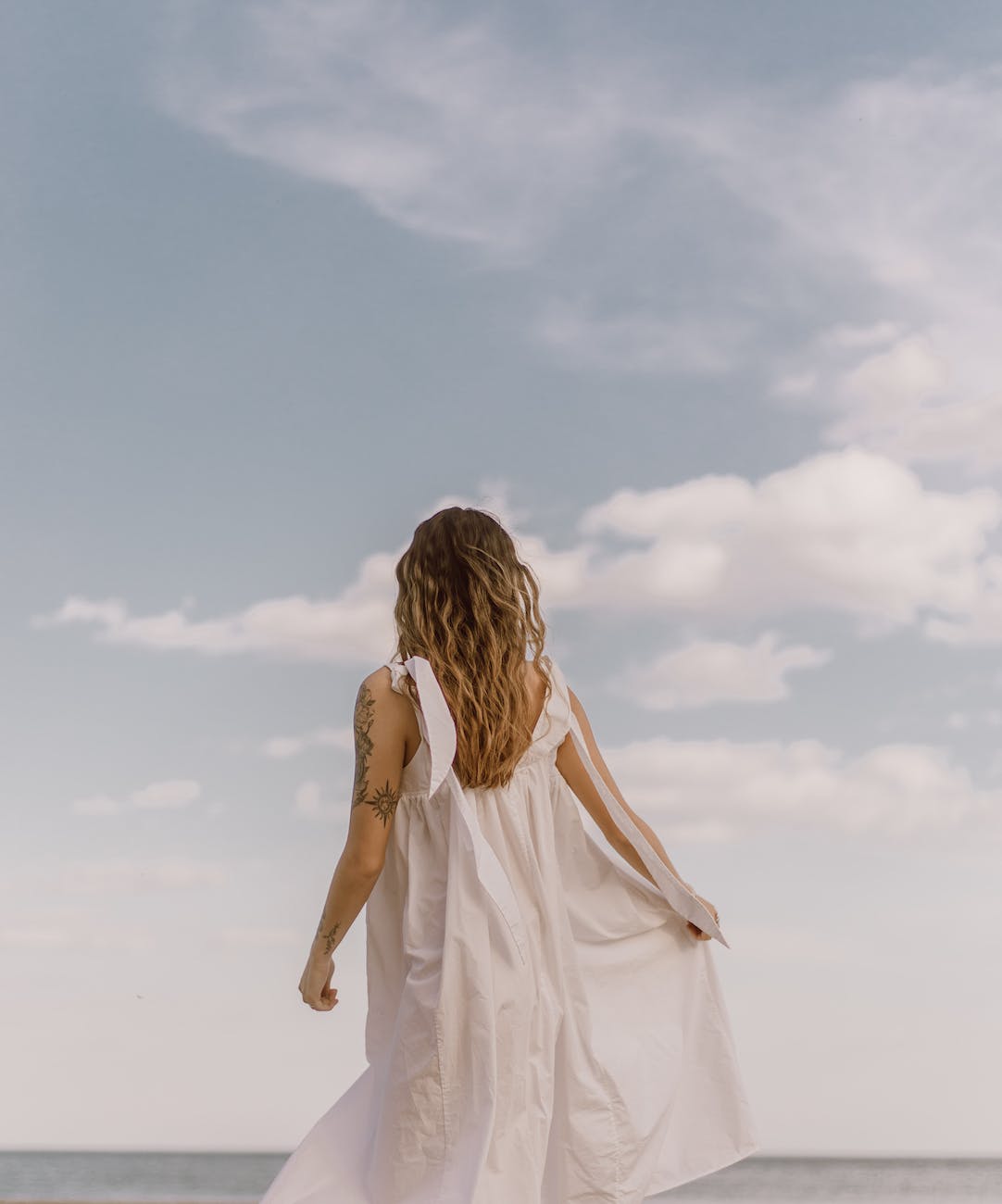 unrecognizable tattooed woman admiring ocean under cloudy sky