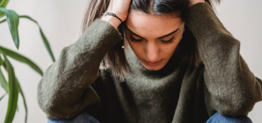 depressed young ethnic lady touching head and looking down sitting near wall