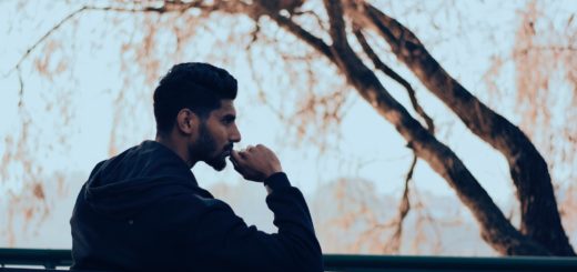 man in black hoodie sitting on bench near green trees