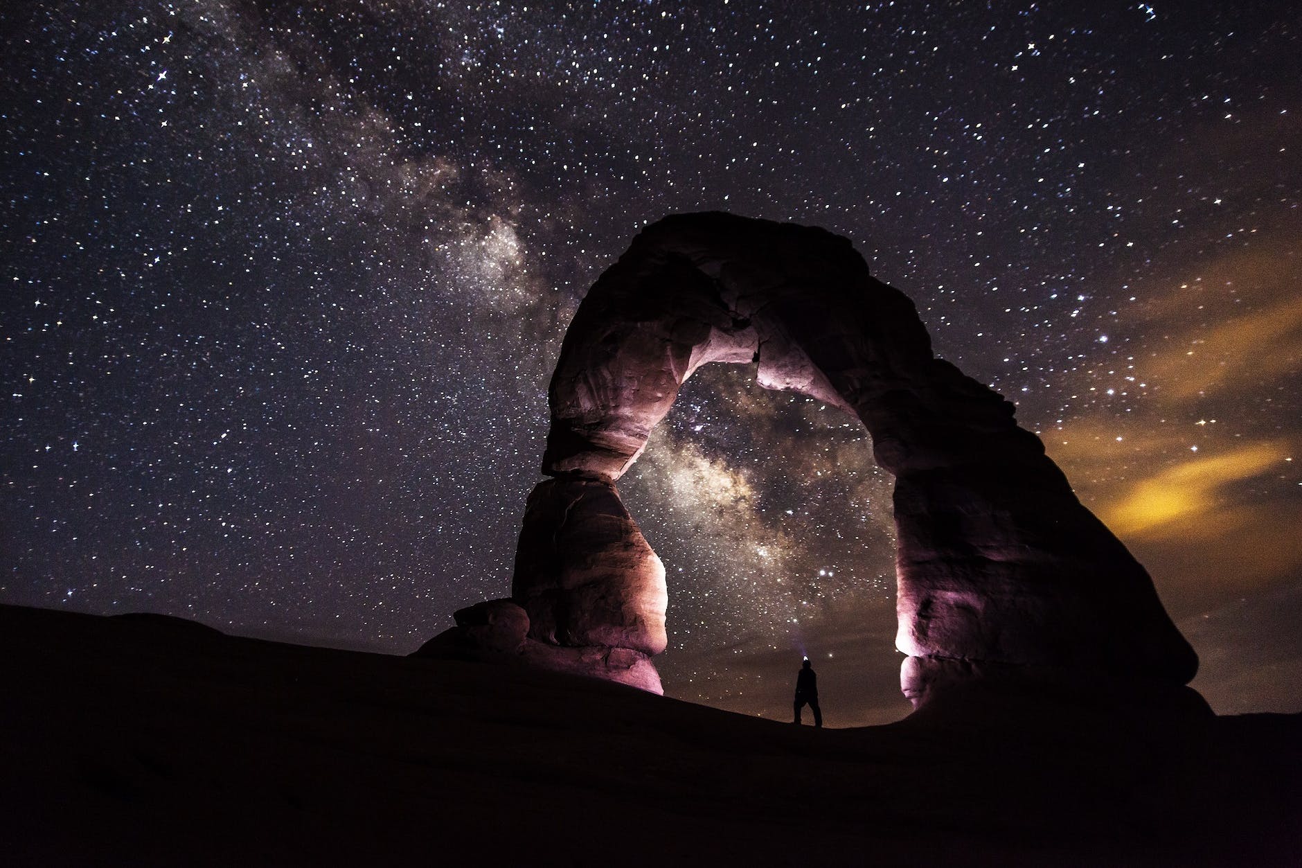 person standing under a rock formation on a starry night