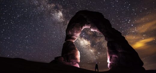 person standing under a rock formation on a starry night