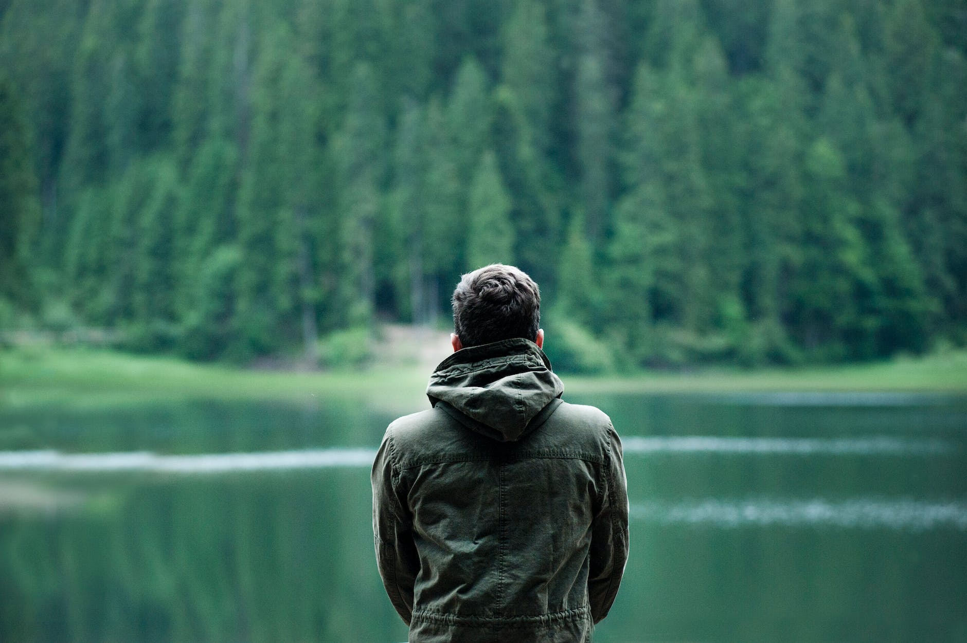 photo of man wearing hooded jacket in front of body of water