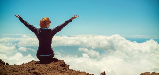 person sitting on cliff raising up both hands