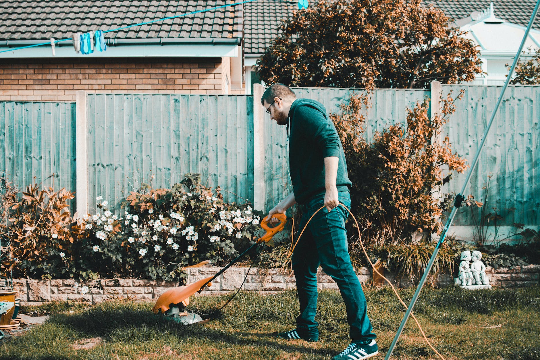 man holding orange electric grass cutter on lawn