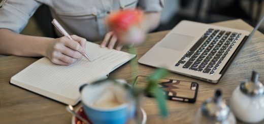 person writing on a notebook beside macbook