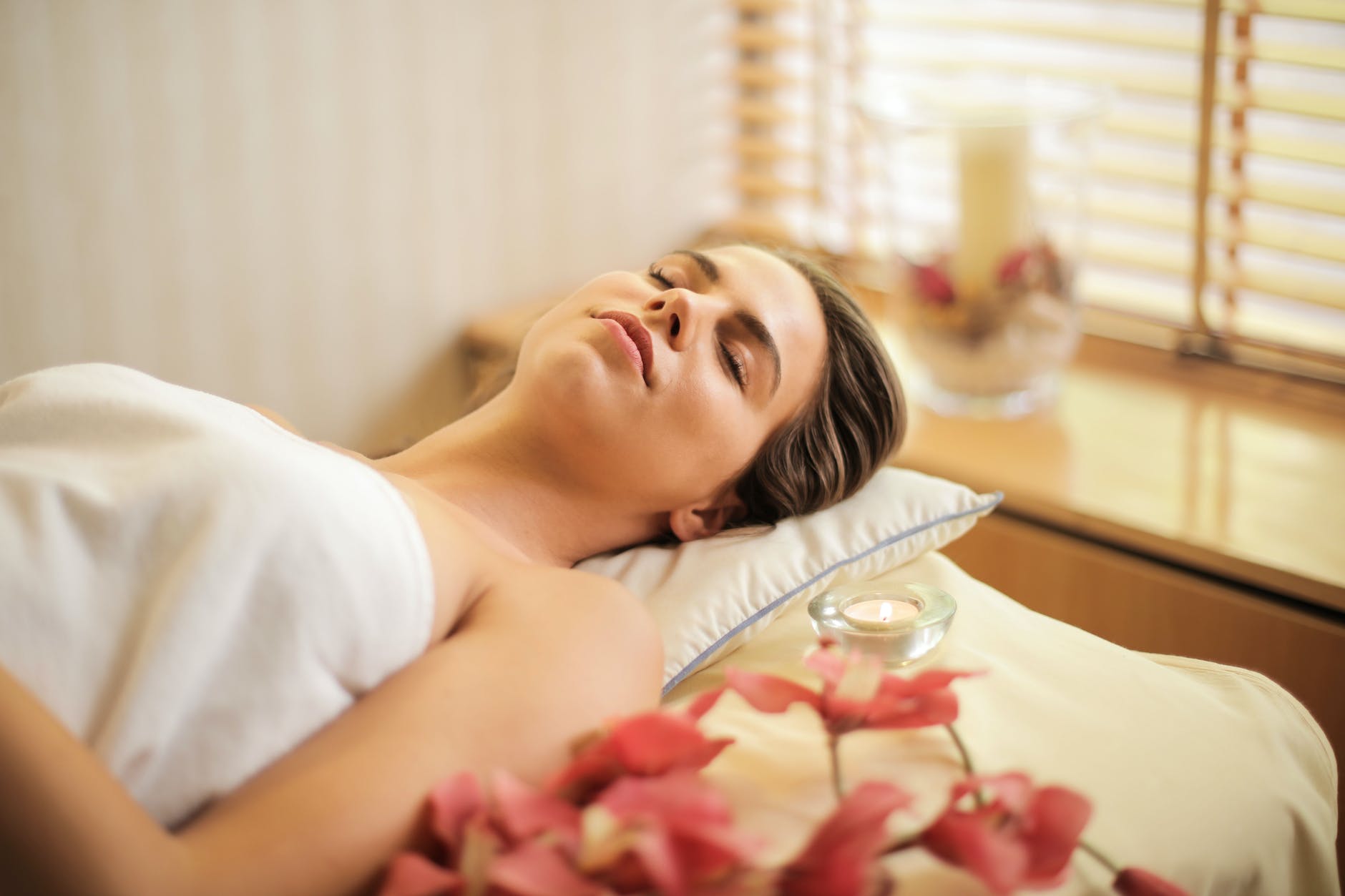 woman in wrapped in white towel lying on bed with eyes closed