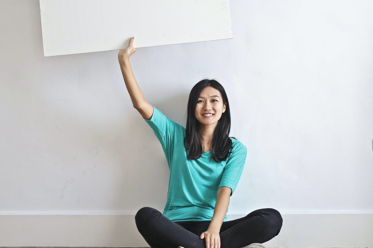 smiling ethnic woman with blank poster in empty flat