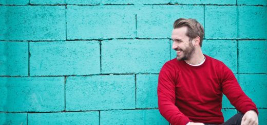 man wearing red sweatshirt and black pants leaning on the wall