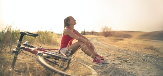 sportive woman with bicycle resting on countryside road in sunlight