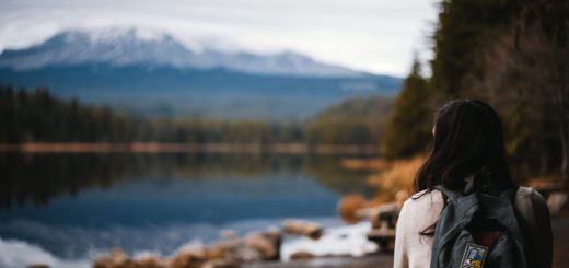 woman in gray jacket standing near lake during daytime