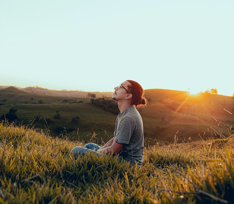 man in white shirt sitting on green grass field during sunset