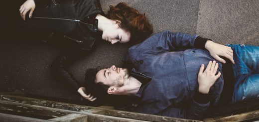 man and woman lying on gray concrete surface looking at each other